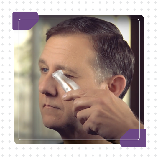 A person uses a small, clear tool on the area under their eye. The image is framed with a black border featuring white plus signs and purple accents in the corners.
