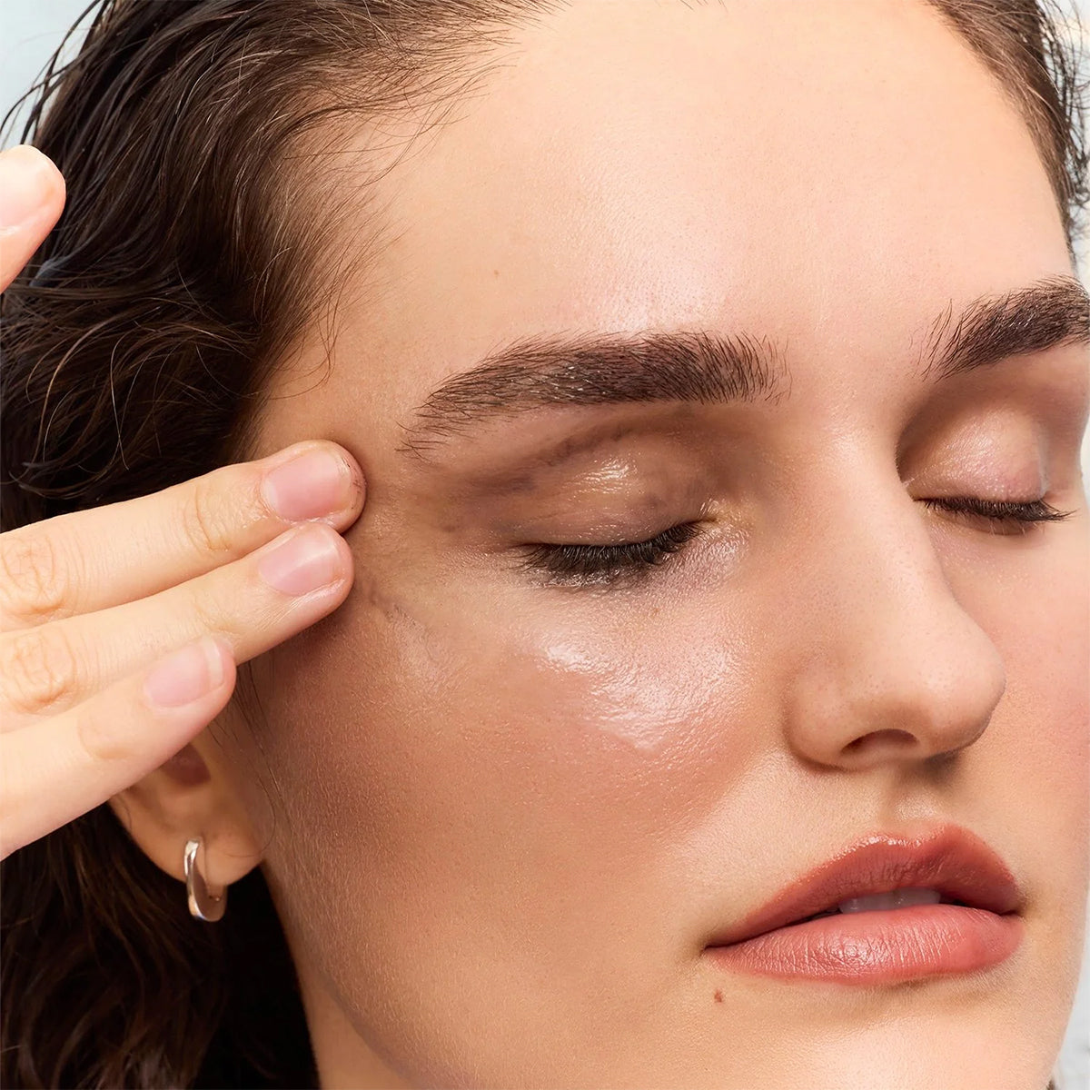 With closed eyes, a person gently touches their smooth, nourished skin under soft lighting. The calmness in their expression showcases the effortless touch of an ophthalmologist-developed routine with the Daily Practice Nourishing Makeup Melting Balm – Effortlessly Clean & Hydrate (70g).