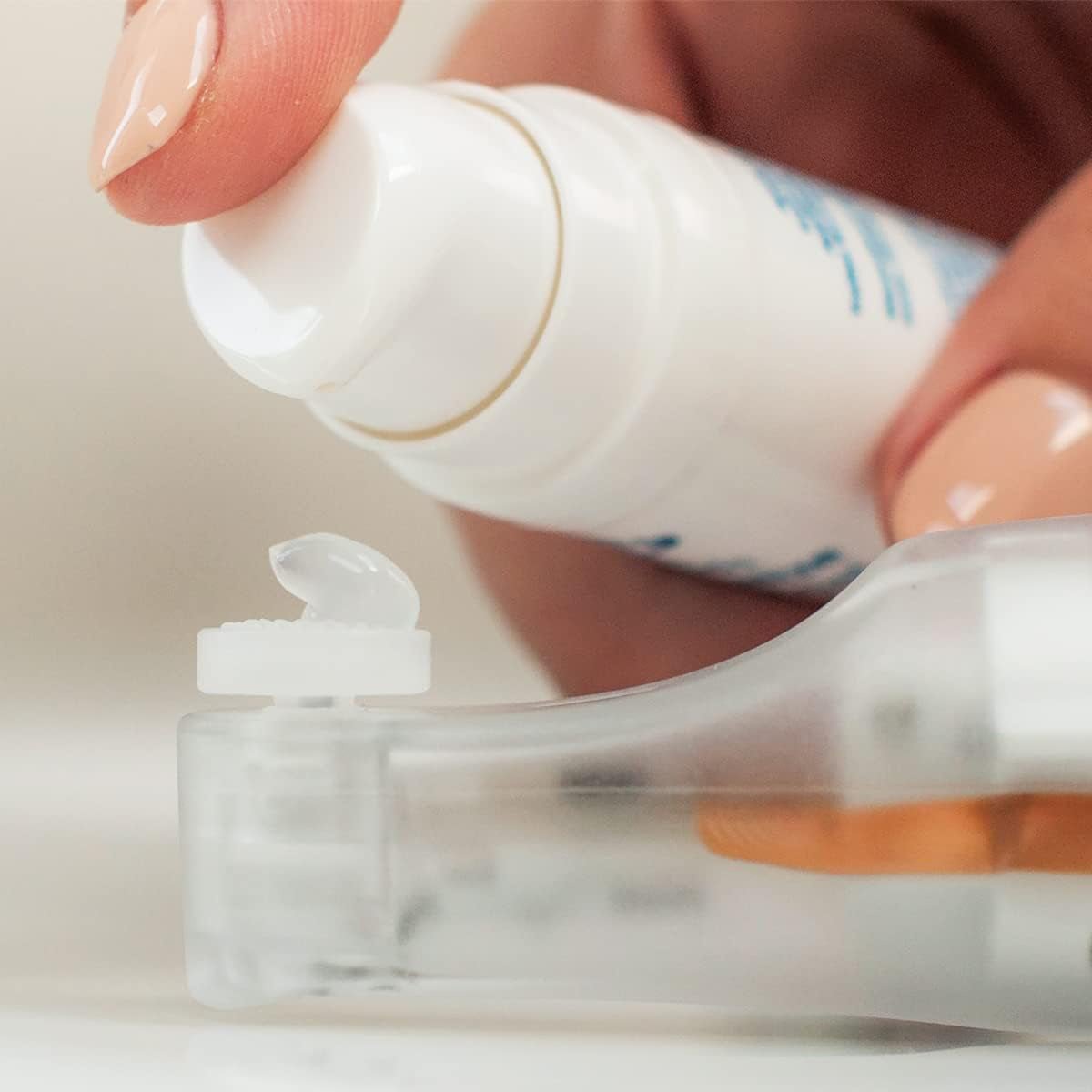 A person presses the pump of a white applicator gel bottle from Nusight Medicals NuLids All Natural At-home Eye Treatment, dispensing clear gel onto a transparent surface. Neatly manicured nails hint at its use as part of the eyelid hygiene system for dry eye treatment.