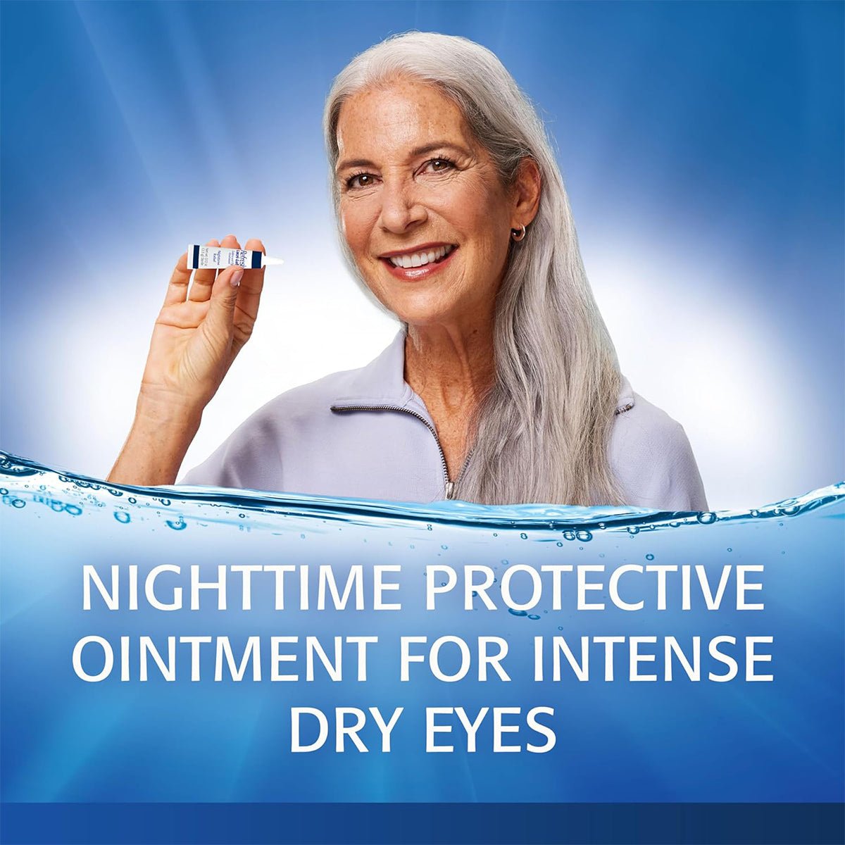 A smiling woman with long gray hair holds a tube of Refresh Lacri-Lube Lubricant Eye Ointment by Abbvie against a blue background. Text reads, Nighttime Protective Ointment for Intense Dry Eyes. Water effect at the bottom.
