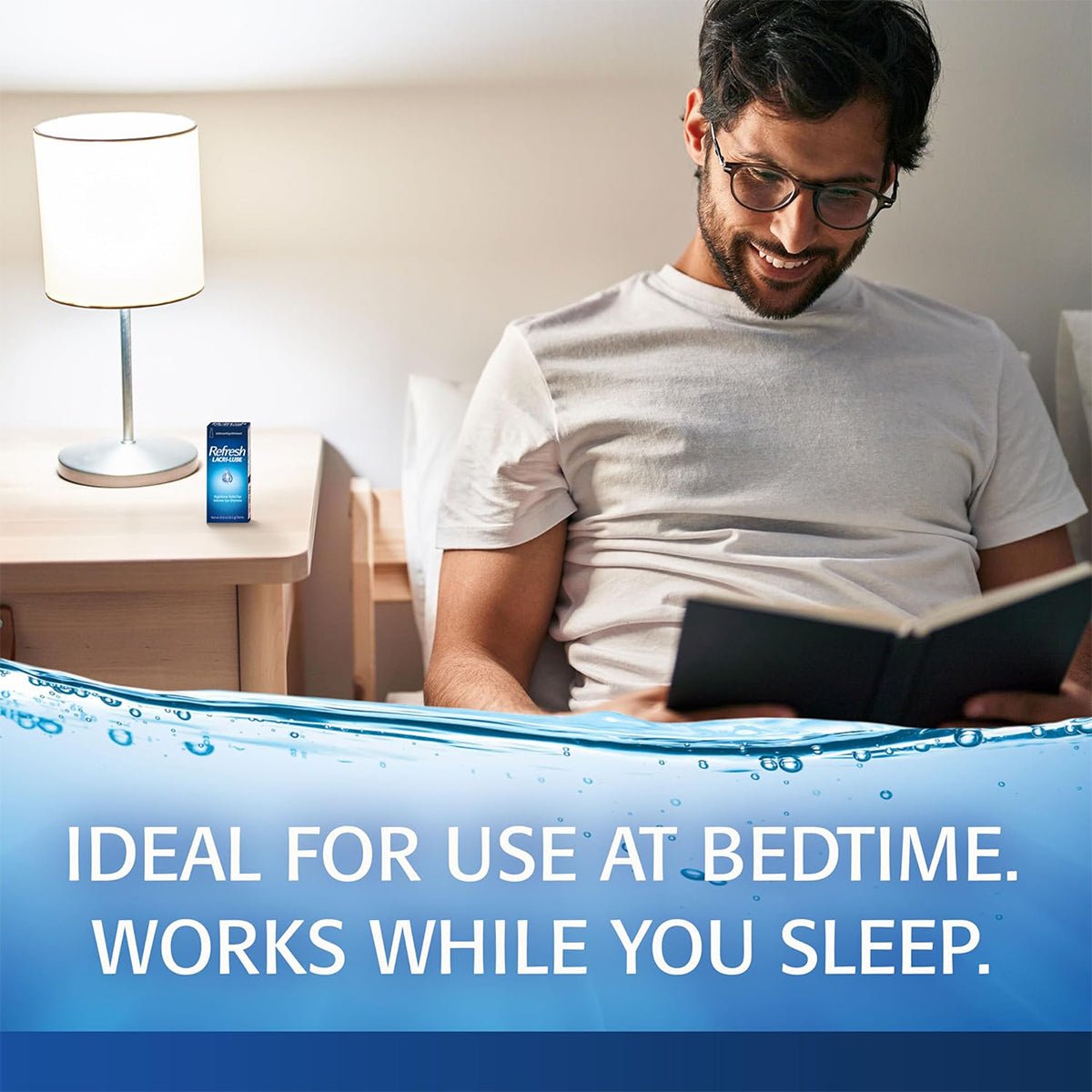 A man with glasses sits on a bed reading, beside a nightstand holding a lit lamp and Abbvies Refresh Lacri-Lube Lubricant Eye Ointment (3.5g tube). Text below states, Ideal for bedtime. Relieves dry eyes as you sleep.