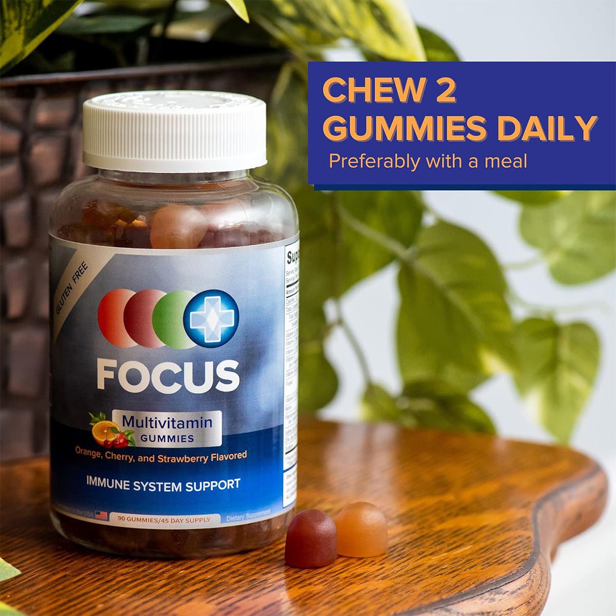 A bottle of Focus Vitamins Multivitamin Gummies to Support Overall Health (90 Ct, 45 Day Supply) sits on a wooden surface, surrounded by greenery. The label highlights orange, cherry, and strawberry flavors for immune support and energy. A note suggests, Chew 2 gummies daily with a meal.