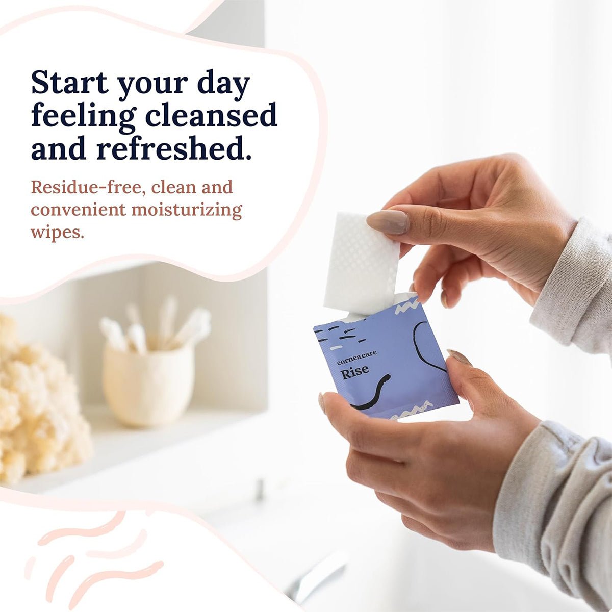A person pulls a moisturizing wipe from a decorative package labeled CorneaCare Wipes with Tea Tree Oil in a bright, white bathroom. Text reads, Feel cleansed and refreshed. Enjoy residue-free, clean, and convenient eyelid hygiene.