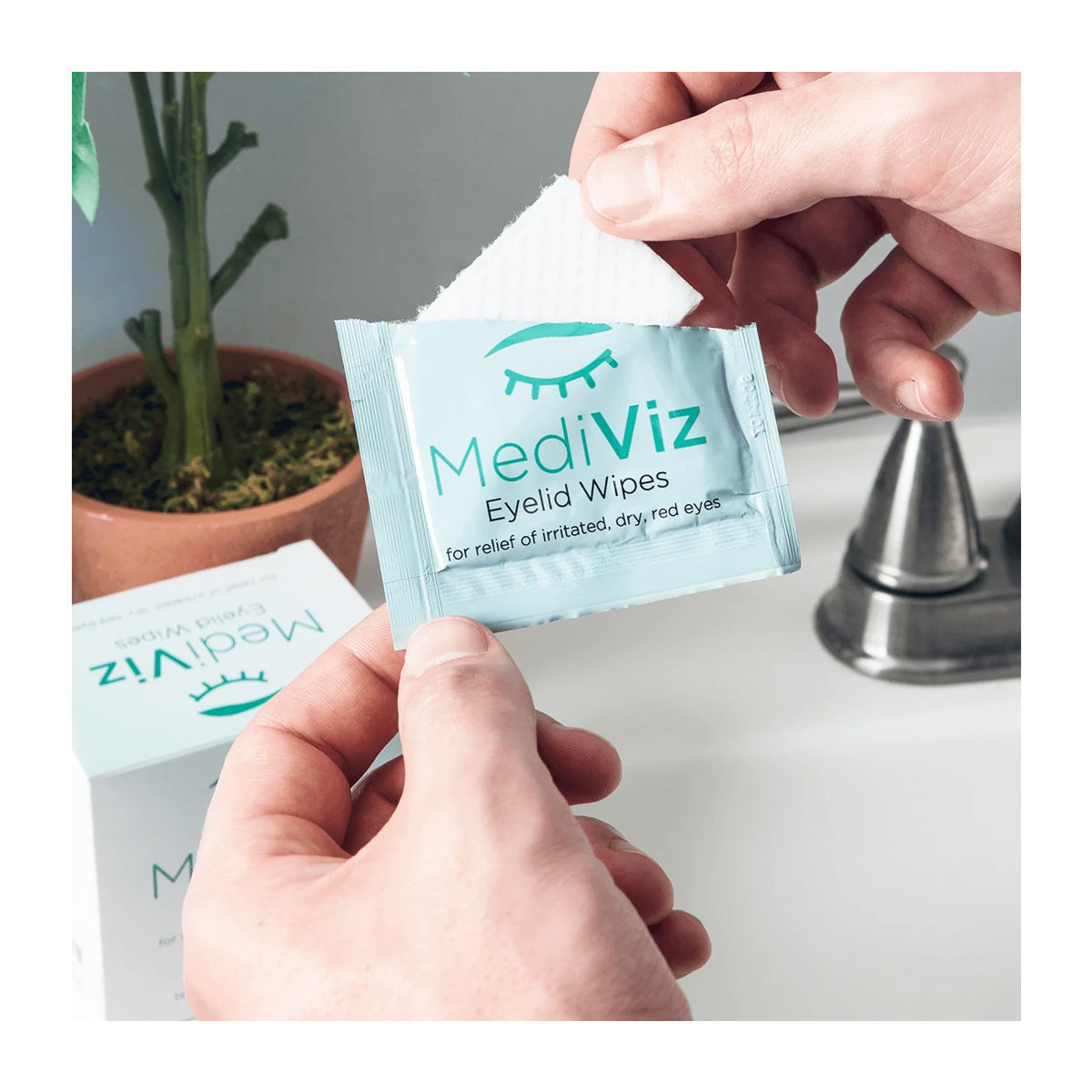 A person holds a MediViz Eyelid Cleansing Wipes (No Tea Tree Oil) packet by PRN, depicted in light blue with an eye illustration. It sits among similar packets with a plant and metal faucet as backdrop, all aimed at promoting optimal eye health.