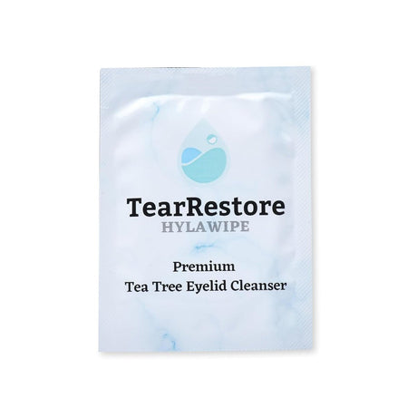 A white packet labeled TearRestore HylaWipe Tea Tree Lid Hygiene Wipes (30ct) features a water droplet and leaf logo. The text says Premium Tea Tree Oil Eyelid Cleanser with Hyaluronic Acid on a light marbled background.