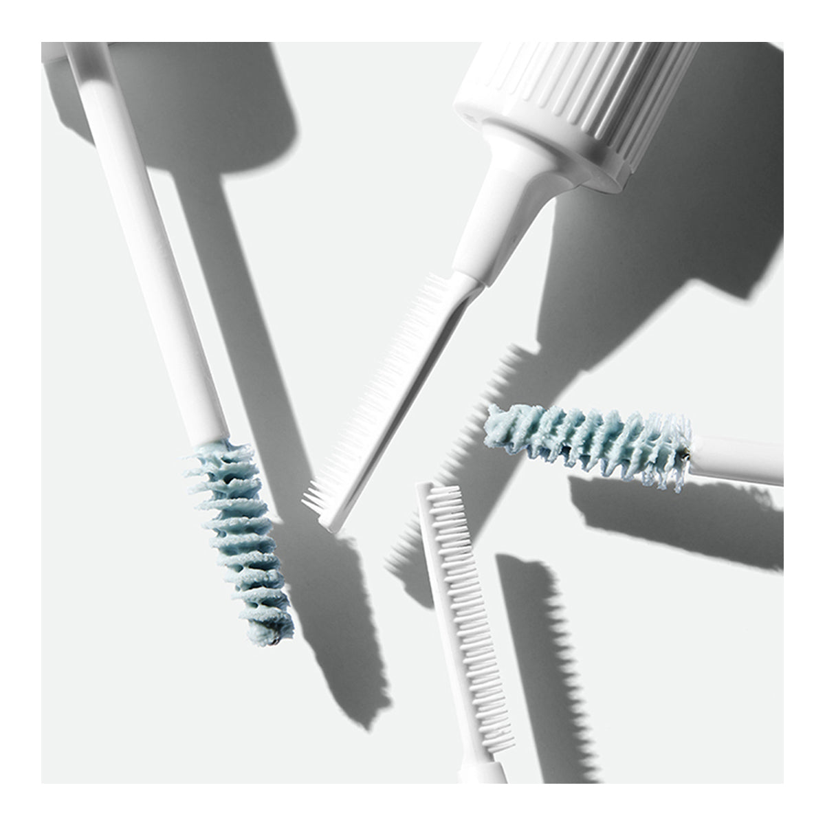 Four white and blue dental brushes and interdental cleaners sit on a light surface with shadows, akin to the precision of RevitaLash Lash and Brow Masque used in meticulous lash or brow treatments.