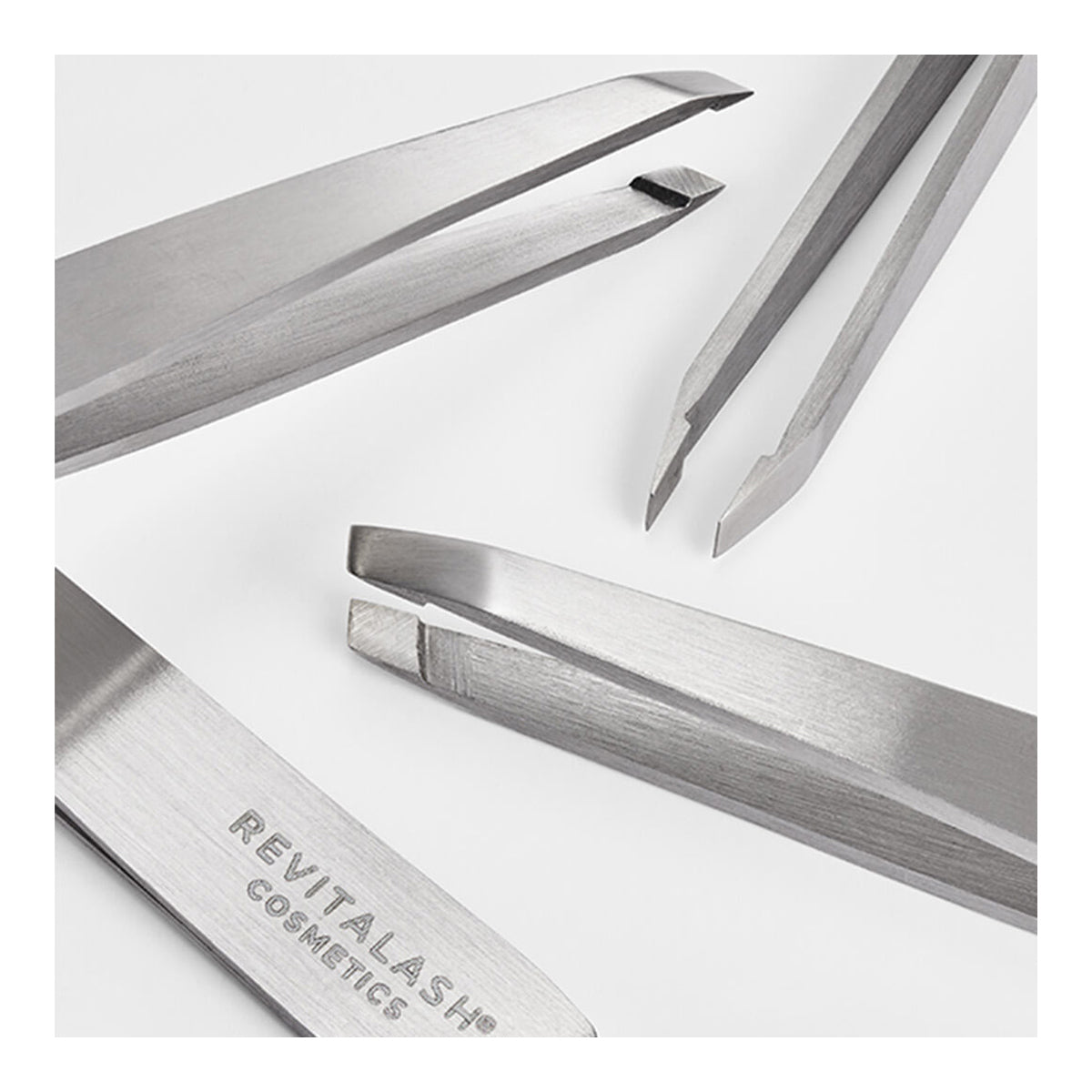 Close-up of four stainless steel tweezers on a white background. One is labeled RevitaLash. The RevitaLash Precision Tweezer set includes slanted, pointed, and straight tips for crafting beautifully arched brows with ease.