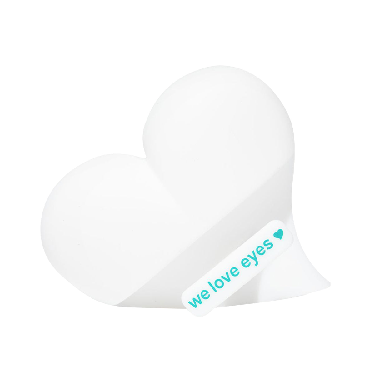 A white heart-shaped object with a diagonal stripe and a we love eyes label in turquoise with a small heart, resembling We Love Eyes Eyelid Scrub Mitt packaging. The plain white background highlights this essential product from We Love Eyes.