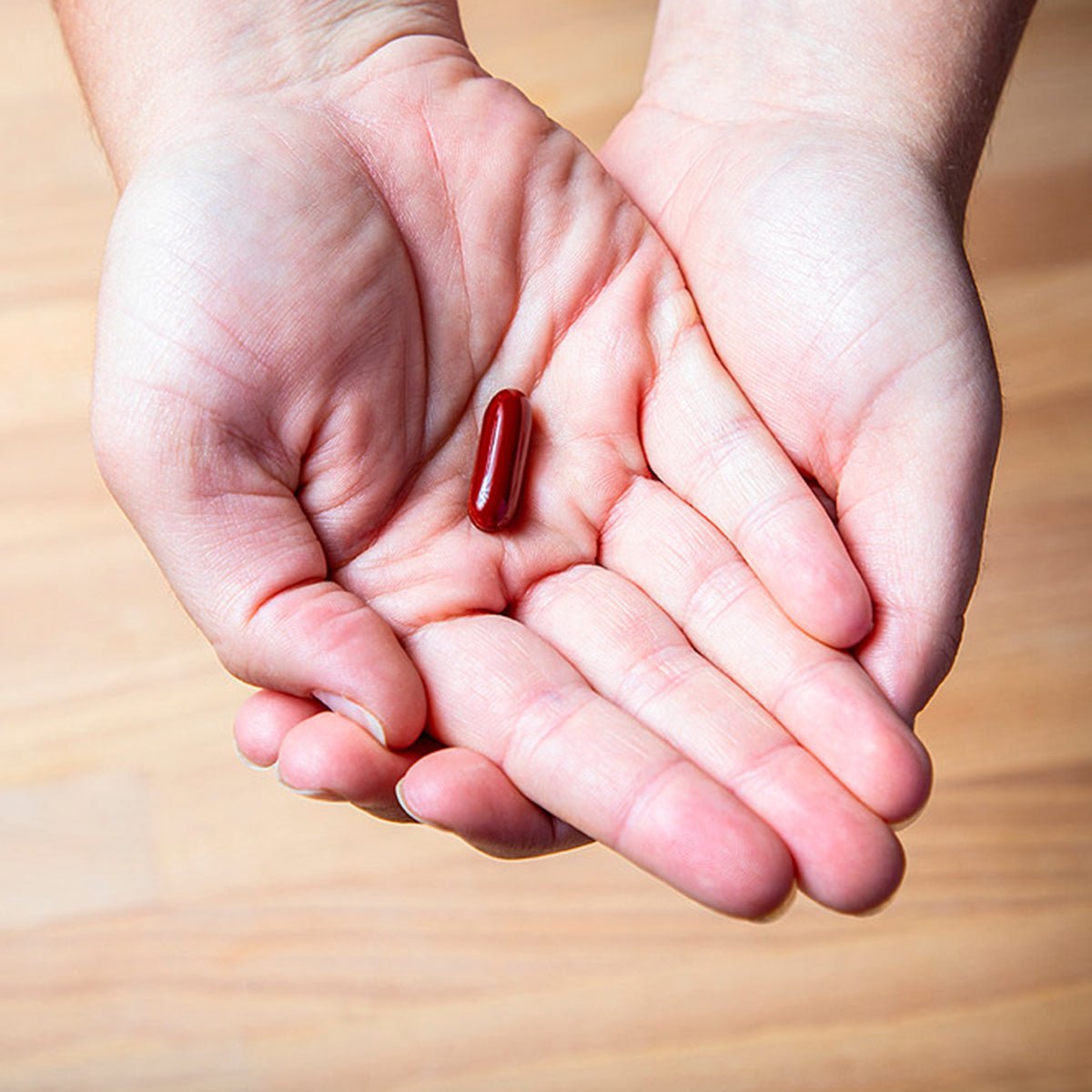 Cupped hands delicately cradle a single red capsule on a light wooden surface, spotlighting EyePromise DVS Eye Vitamin. This supplement, intended for retinal support in diabetic retinopathy, naturally promotes blood sugar health.