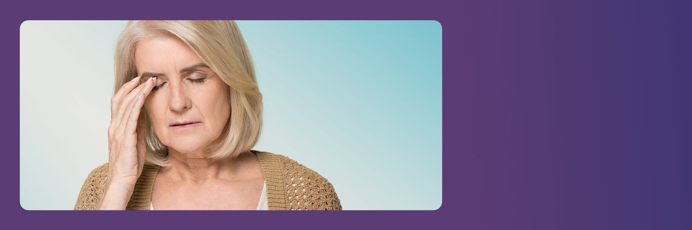 An older woman with shoulder-length blonde hair is touching her forehead with a hand, eyes closed, appearing to have a headache or be in deep thought. Shes wearing a beige knit cardigan against a blue gradient background.
