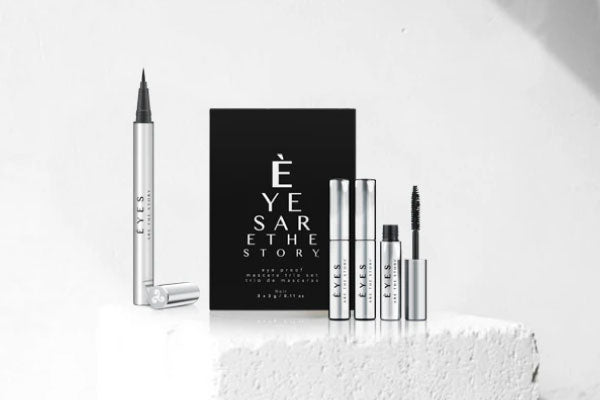 A sleek set of silver and black eye makeup products displayed against a white background. Includes an eyeliner pen, mascara tube, and packaging with the text EYES ARE THE STORY.