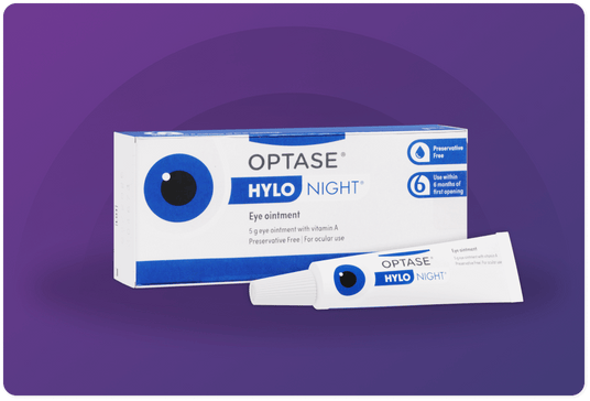 Image of a rectangular box of OPTASE HYLO Night eye ointment with an image of an eye on it, against a purple background. The ointment tube is placed in front of the box. Text indicates it is preservative-free and for use within six months of opening.