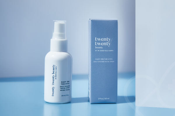A white spray bottle labeled twenty twenty beauty stands next to its matching light blue box. The products are on a blue surface against a light background, with soft lighting highlighting the packaging.