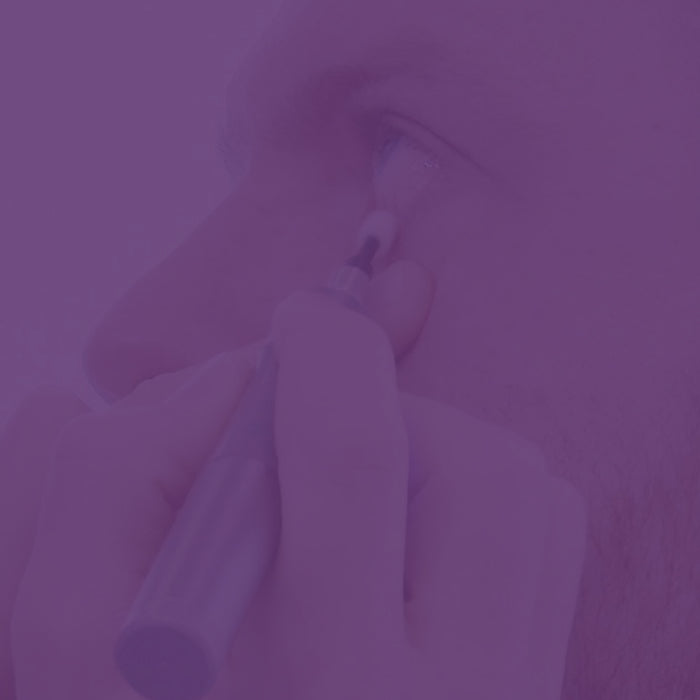 A person applies makeup to their eyelid using a brush or pen. The image has a purple tint, making details less distinct. The persons eye is open, and their facial features are partially visible.