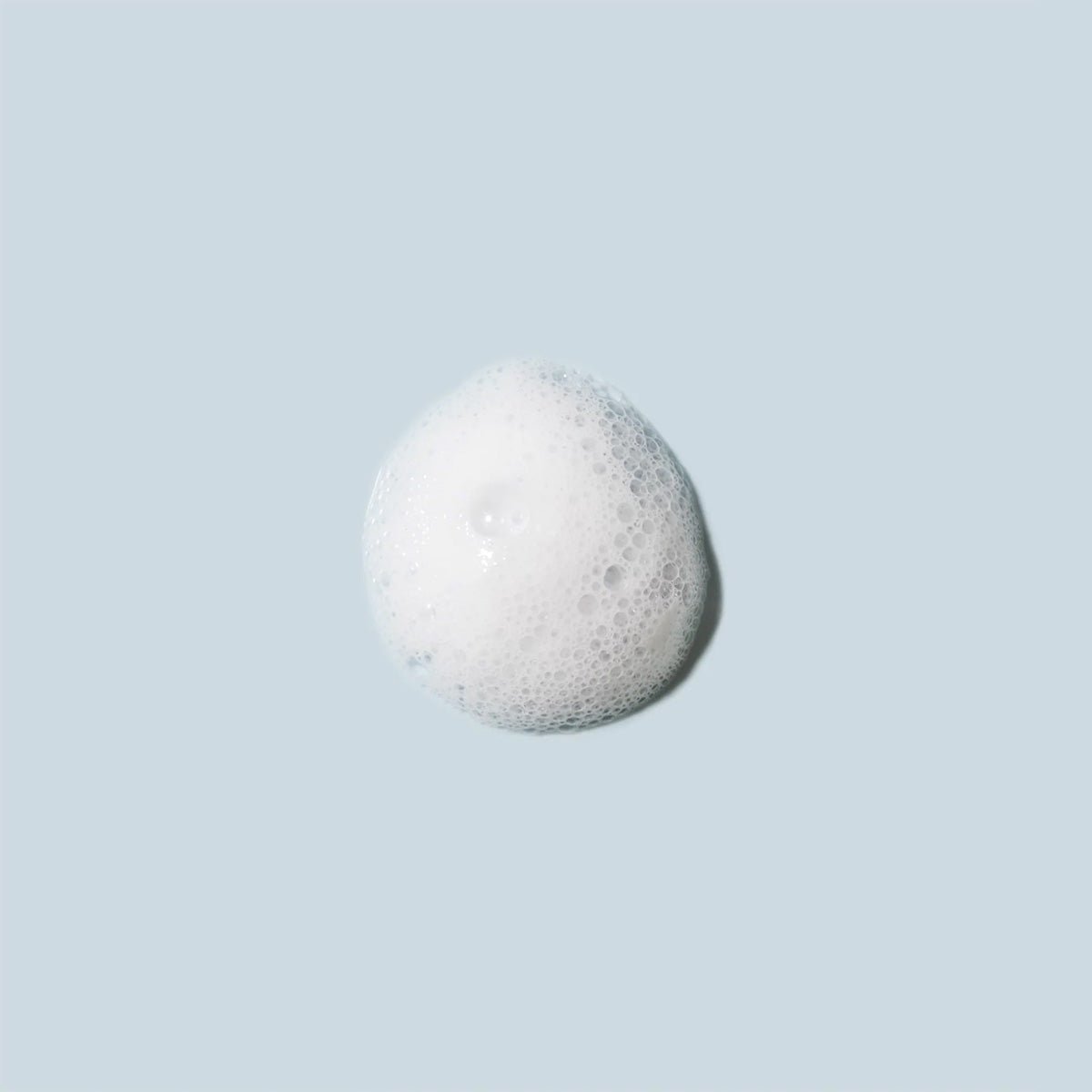 On a light blue background, a small round cluster of white foam bubbles evokes the gentle touch of Daily Practice’s 80mL Purifying Foam Cleanser, perfect for hydrating the sensitive eye area and lashes.