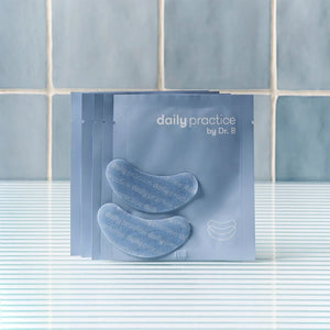 Five blue packets of Daily Practice Brighten & Hydrate Eye Patches – Instantly Refresh & Rejuvenate Your Eyes (5-Pairs) are fanned out on a striped surface, featuring two crescent-shaped patches for reducing puffiness and dark circles. A tiled wall serves as the backdrop.