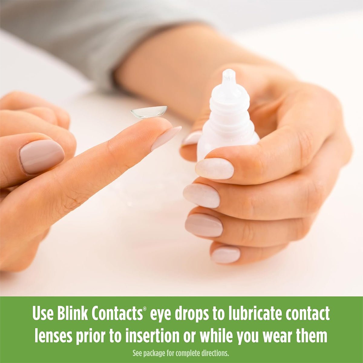 A person with manicured nails holds a contact lens, about to apply lubricating eye drops. Text below suggests using Bausch + Lombs Blink Contacts Lubricating Eye Drops (10ml) for added comfort before or during wear.