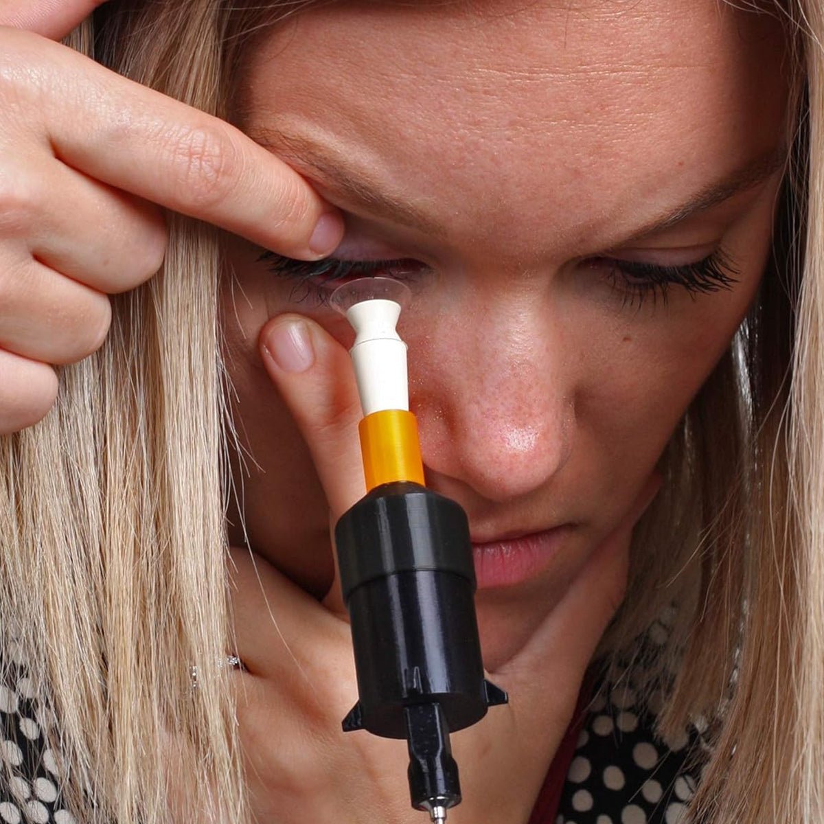 Using Augmented Vision Labs sleek S5 Inserter, users apply drops into their eye, holding it close and pulling down on their lower eyelid. The black applicator with a white and orange dropper provides precision and comfort during lens insertion coaching. Includes free video training for scleral & hybrid lenses.