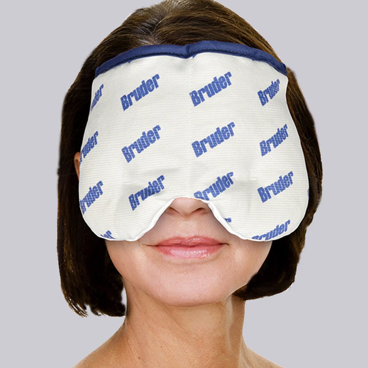 A person uses a Bruder Moist Heat Sinus Compress with blue trim for sinus relief. The white mask, featuring Bruder in blue, covers their eyes, set against a plain gray background.