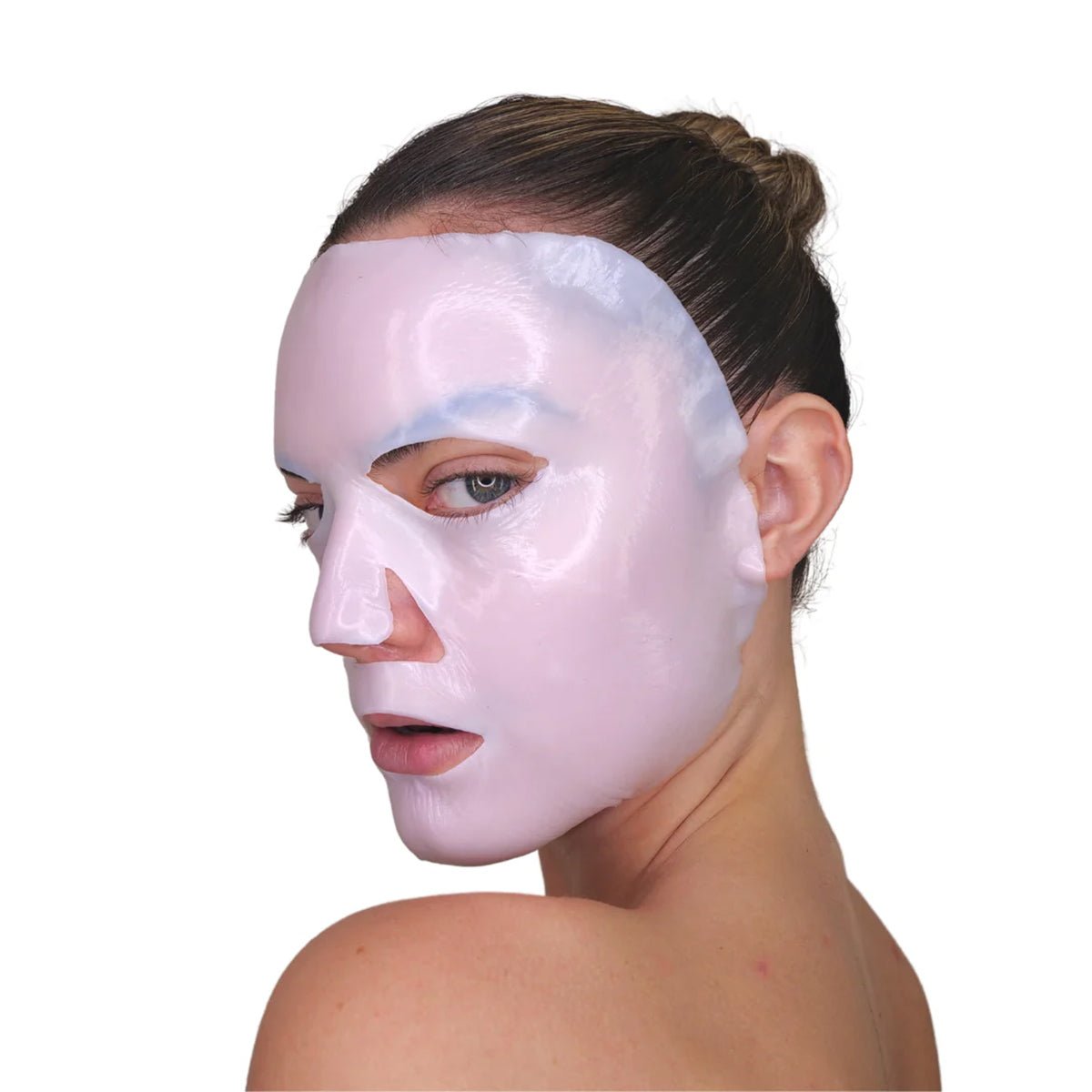 With hair tied back, a person glances over their shoulder wearing a glossy, light pink Velez Intense Hydration Cellulose Face Mask. The white background highlights the masks sheen and suggests its advanced skin regeneration and hydration benefits.