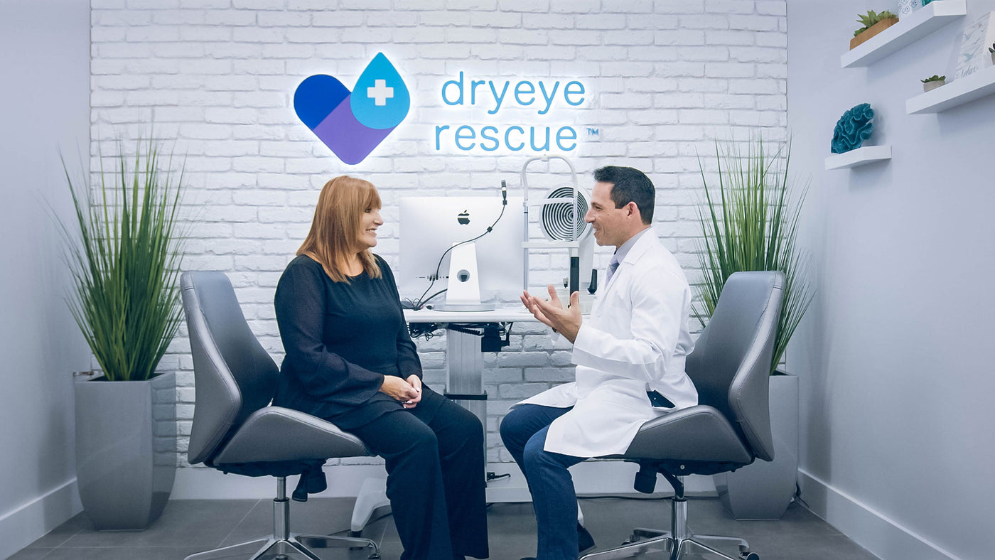 A woman and a man in a lab coat sit facing each other in a medical office with modern decor. On the wall behind them is a logo reading Dry Eye Rescue. Medical equipment is visible between them.