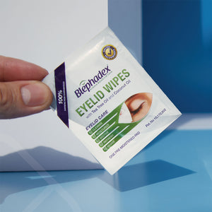 A hand holds a Lunovus packet labeled Blephadex Eyelid Wipes with Tea Tree and Coconut Oil, emphasizing eyelid hygiene. The serene packaging features a closed eye and promises soothing with tea tree and coconut oil, set against a calming blue background.