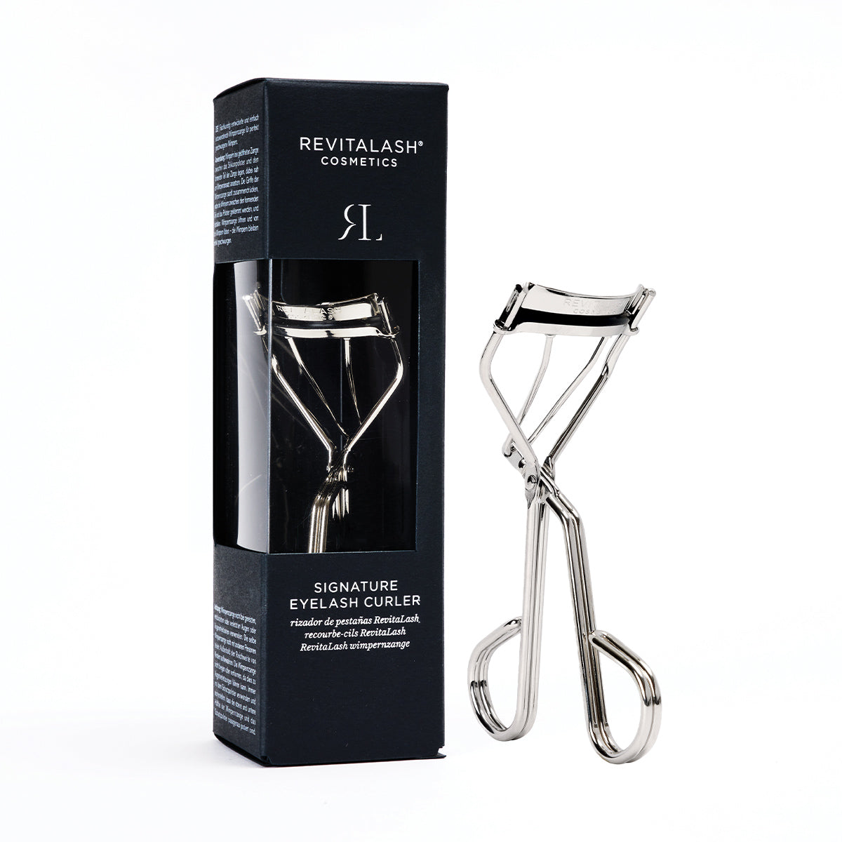 The RevitaLash Signature Eyelash Curler, made of carbon steel, is showcased with its stylish black packaging. It includes silicone pads for comfort and a clear window to highlight the curlers metallic design.