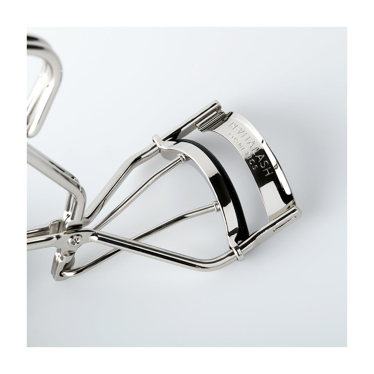 Close-up of the RevitaLash Signature Eyelash Curler, made of carbon steel with black silicone pads, engraved with HVW LASH, set against a plain white background.