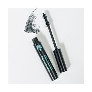 An open We Love Eyes Lashfull Thinking BLACK Pressed Serum Mascara tube, with its wand beside it, leaves a bold swipe on the white surface. The wand is coated with volumizing mascara enriched with botanical ingredients. The text on the tube reads We Love Eyes.